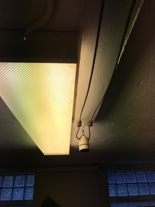 Svart elektrisk ledning som går till en tänt fyrkantigt taklampa med frostad glasruta i bakgrunden.