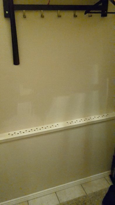 Vägg med svart hängare och krokar, vit sliten bänk, smutsiga golvplattor, tom och oanvänd hörna.