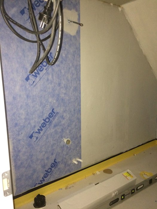 Hörn av ett oavslutat badrum med vägg våtrumsskiva, synliga VVS-rör och lutande vattenpass under renovering.
