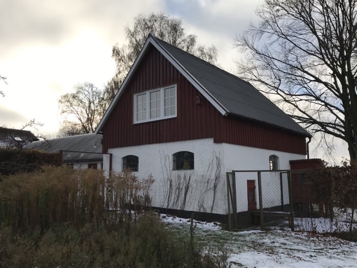 Nymonterat stort PVC-fönster på ett tvåvåningshus med röd panel och snö på marken.