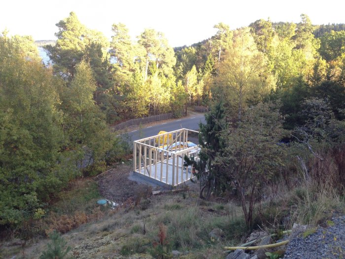 Garagegrund med kantelement på en byggplats omgiven av natur och en väg i bakgrunden.