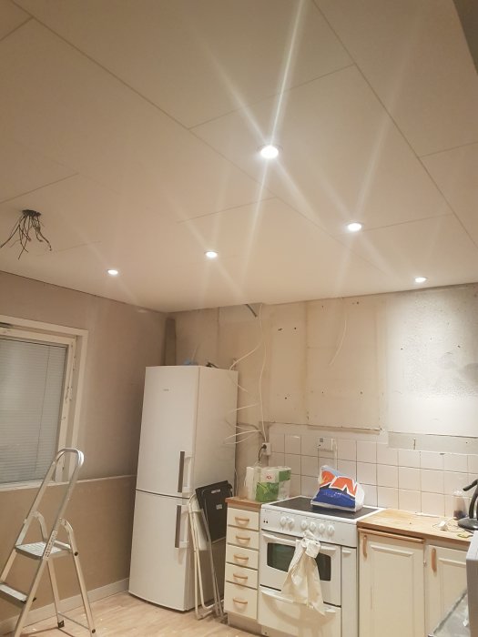 Nyinstallerade spotlights i ett kök under renovering med tända lampor som lyser upp det nymålade taket.