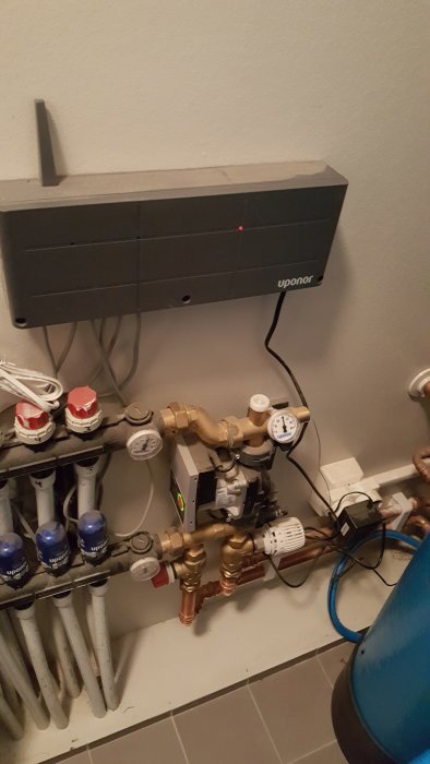 Uponor golvvärmefördelare och termostater anslutna till värmesystem med synliga rör och kablar.