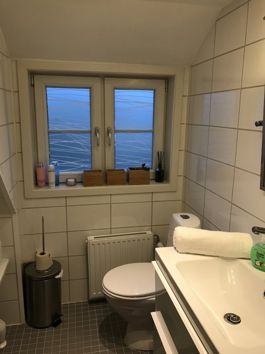 Ett badrum med vita kakelväggar, toalett, badkar, fönster med utsikt och radiator.