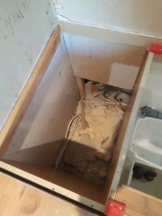 Hörnet av ett kök under renovering med OSB-skivor och gips installerade bakom en diskbänk, exponerade rör och kablar.