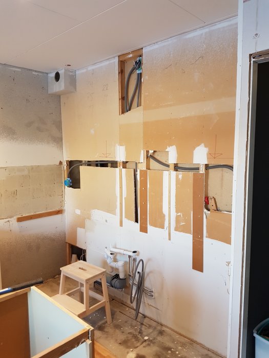 Vägg under renovering i kök med nyinstallerad OSB och gips nära vattenslangar och elledningar.