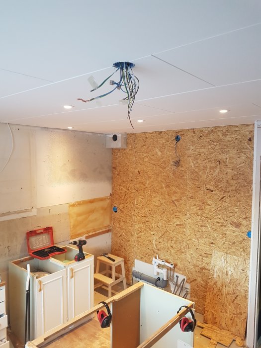 Kök under renovering med nyinstallerade OSB-skivor och renoveringsgips på väggen, oavslutad elektrik i taket.