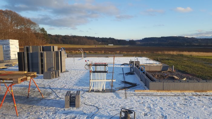 Grundläggning av hus med betongblock och armeringsjärn på snöbeklädd mark.