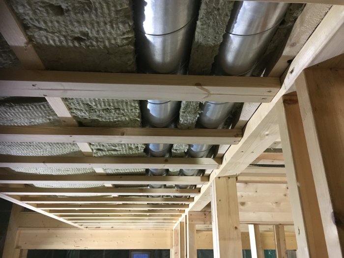 Ventilationsrör i taket med isolering av lös ull mellan träbjälkar under en renovering.