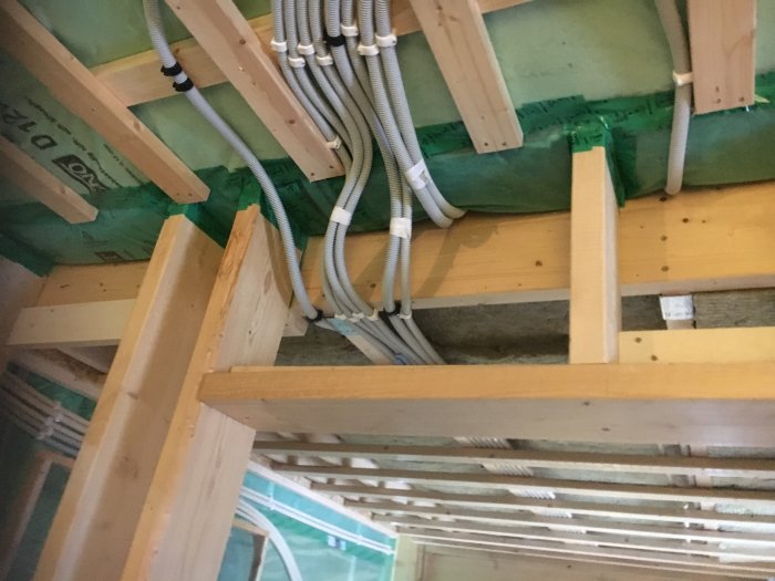 Installation av ventilation med synliga isolerade slangar och lös ull mellan träbjälkar i ett pågående byggprojekt.