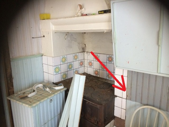 En gammal vedspis inskjuten i väggen med tillhörande köksinredning i behov av renovering.