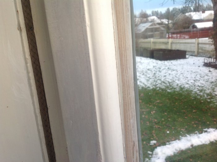 Nahaufnahme eines älteren Fensterrahmens mit einem eingezogenen Dichtungsschnur und Blick auf schneebedeckten Garten.