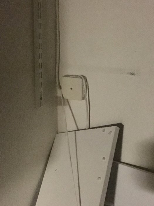 En äldre lysrörsarmatur på en vägg ovanför en vit dörr, med sladdar som sticker ut.