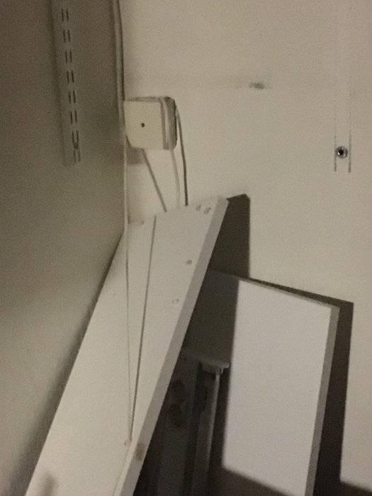 Eluttag och lysrörsarmatur monterade på vägg ovanför lutande trähylla.