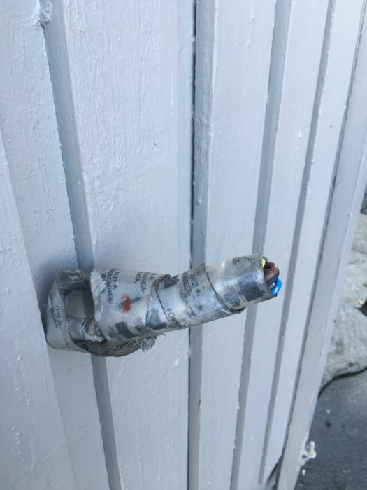 En odefinierbar föremål insvept i tidningspapper sticker ut från en vitmålad trävägg.
