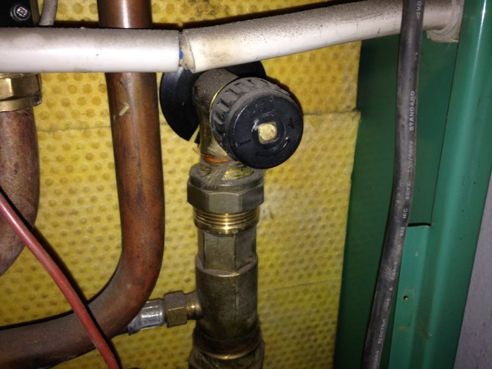 Rörinstallation med flödesvakt, pump, värmeväxlare och avstängningsvred mot en isolerad vägg.