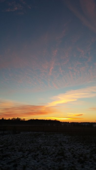 Solnedgång med dramatiskt orange och rosa himmel över snötäckt landskap.