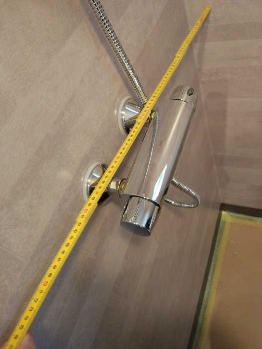Mätning av duschblandarens utstick med måttband i badrum, blandaren sticker ut 8 cm från väggen.