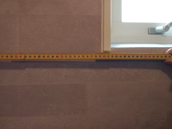 Måttband visar avståndet mellan duschblandare och vägg i ett badrum.