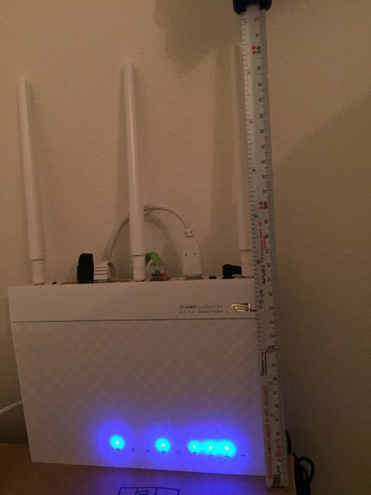 En vit trådlös router med tre antenner bredvid en meterstock som visar höjden 31,5 cm.