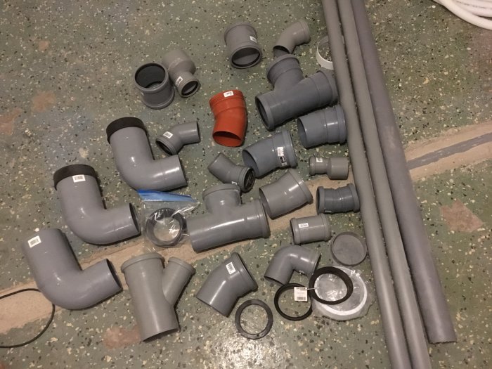 Olika nya och en använd avloppskomponenter av plast spridda på ett verkstadsgolv.