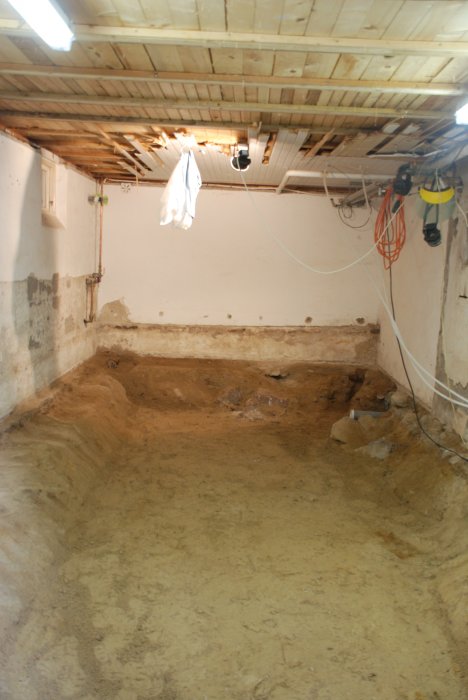 Utsikt över en källargrund under renovering med grävd ur jord och synliga stenar samt murverk.
