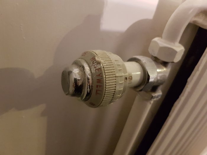 Slitet termostatventil på en radiator med texten 'Honeywell' söker råd för underhåll eller byte.