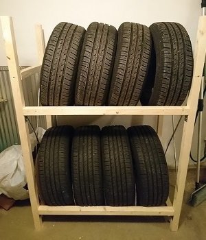 Hemmagjort däckställ av träreglar med två hyllplan fulla av bilddäck, placerat i ett garage.