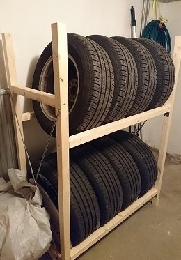 Hemmagjort däckställ i trä med två hyllplan fyllda med bildäck, står i ett garage.