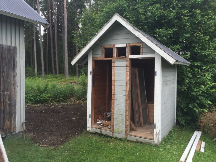 Ett litet grått hus i en grönskande trädgård, används i bygget av en hundgård.