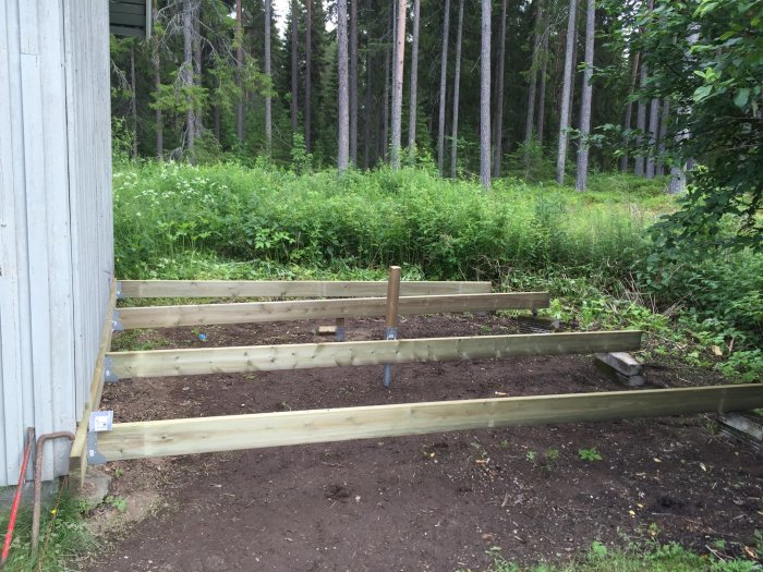 Grundkonstruktion av en hundgård i skogsmiljö med träramar placerade på marken vid sidan av en byggnad.