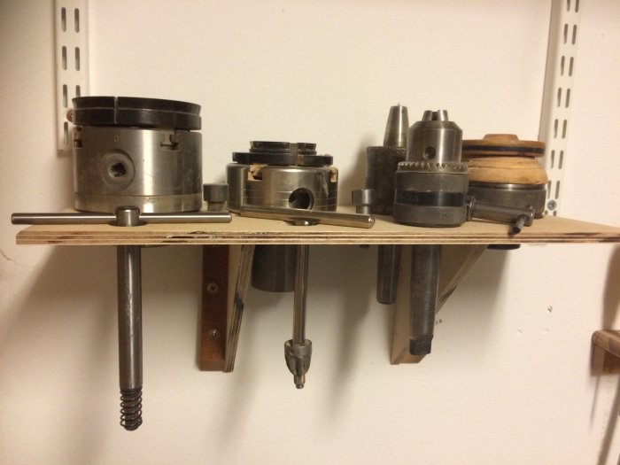 Hylla på vägg med metallchuckar för svarv och verktygsstång undertill.