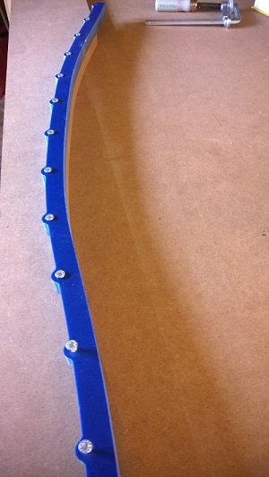 MDF-skiva med utfräst båge och guide anfäst med skruvar, används som mall för karmöverstycken.