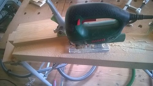 En överfräs från Bosch används på ett träöverstycke fäst i en arbetsbänk med spån som resultat av bearbetningen.