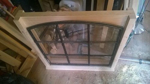 Bågformad dörrkarm i trä under tillverkning med mall och MDF-spån i en verkstad.