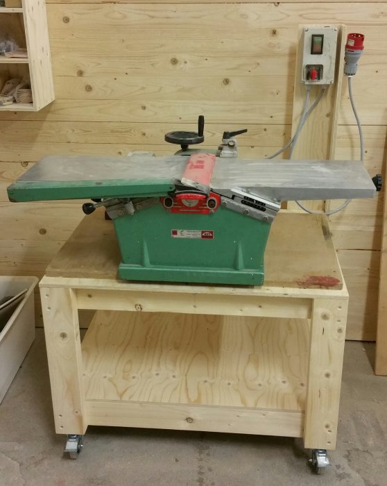 En rikt- och planhyvel monterad på en egenbyggd rullbänk av trä i en verkstad.