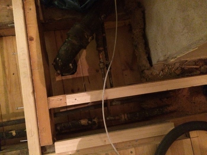 Öppet golv med synliga kopparrör vid en T-korsning som behöver pluggas under renovering.