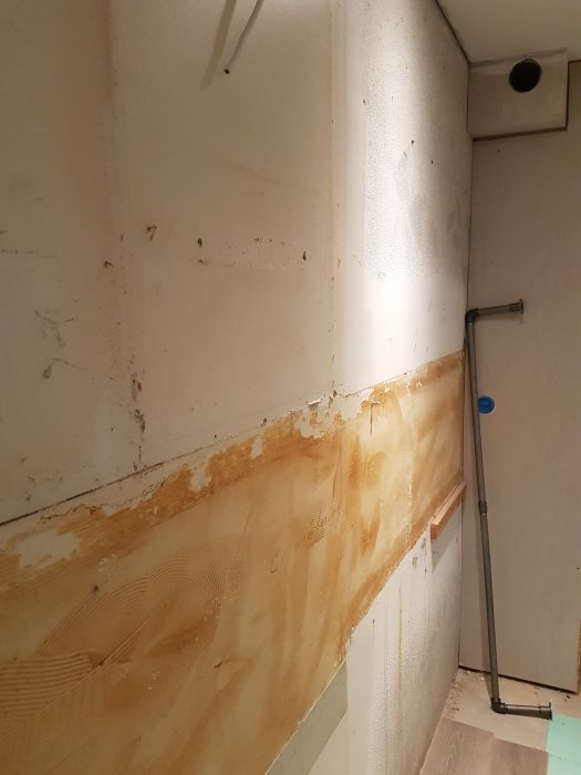 Betongvägg och träplank med rester av bortriven plastmatta och lim, redo för kakling.