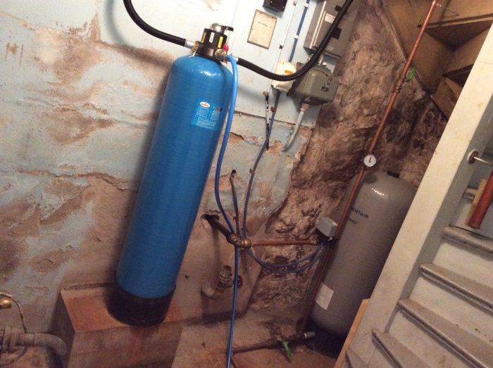 Vattenfiltreringssystem med blå tank och ledningar i ett källarutrymme under renovering.