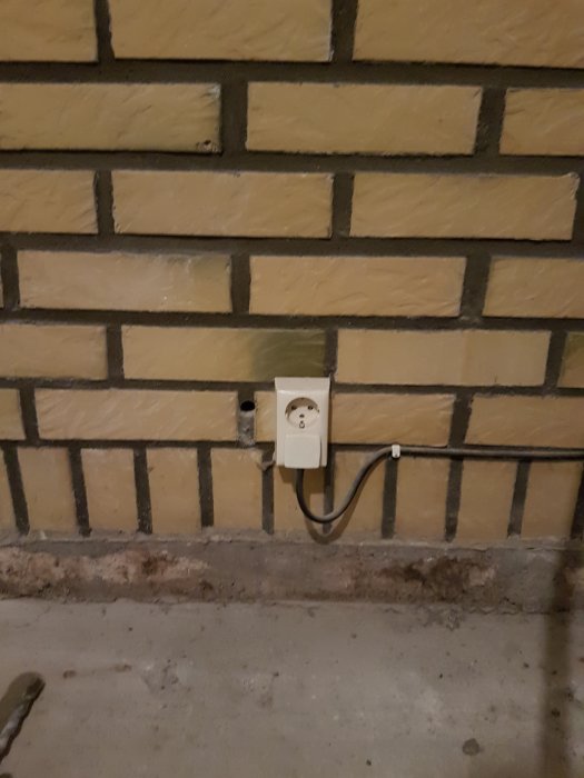 Vägguttag med kabel längs tegelvägg och gammal flexslang på golvet som exempel för förfrågan om elinstallation.