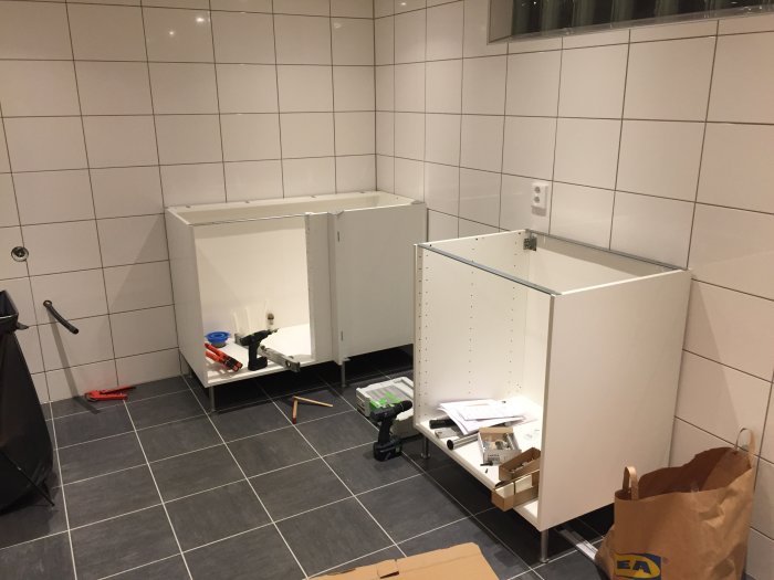 Tvättstugerenovering med pågående montage av vita Ikea-skåpstommar, verktyg och förpackningsmaterial.