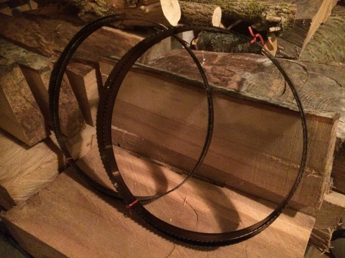 Två nya bandsågsblad ligger på en vedhög, ett bredare 25mm 3tpi och ett smalare 16mm 4tpi.