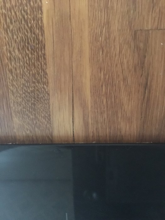 Träpanel med synlig skarv mot en mörk, reflekterande yta, möjligen golv eller bord.