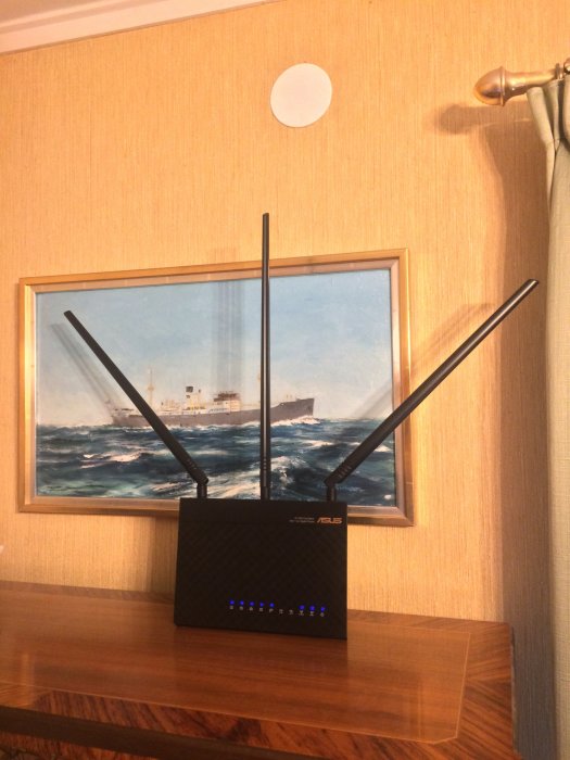 ASUS RT-AC68U-router med utbytta långa antenner placerad framför en tavla på en vägg.