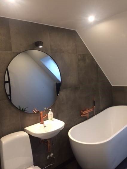 Renoverat badrum med frittstående badkar, spegel ovan handfat med förskjuten lampa och högt placerad handdukstork.