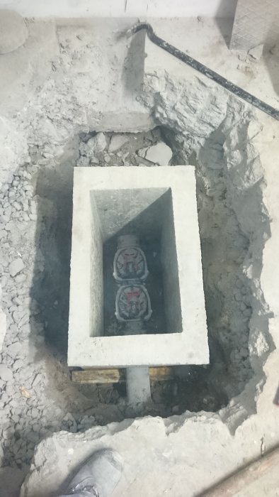 Uppgrävd grop med nygjuten betongform som innehåller två avstängningsventiler för rörledningar.