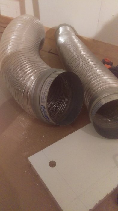 Två flexibla metallslangar med muffar på ett bygggolv, redo för justering i köksrenovering.