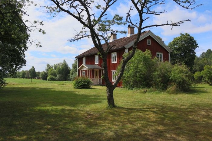 Rödmålat trähus med vita knutar, troligen från 1800-talet, omgivet av en lummig trädgård.