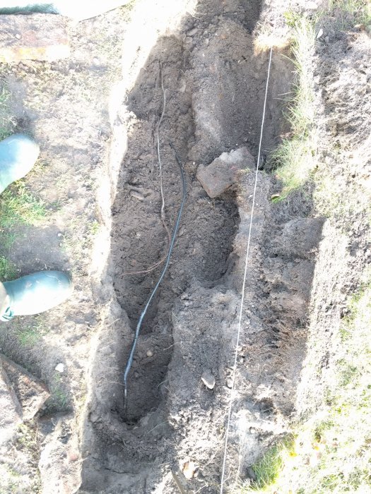 Uppgrävd jordgång med en gammal kabel och tegelsten synlig, cirka 30 cm ner, illustrerar platsen för en skarvning.