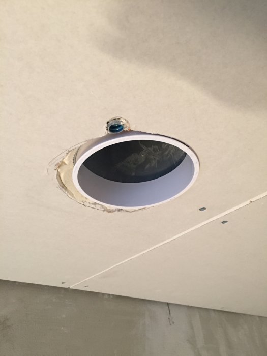 Ojämnt utsågat hål i gipstaket för installation av ljuskopp, med synlig ventilationsrör-koppling.